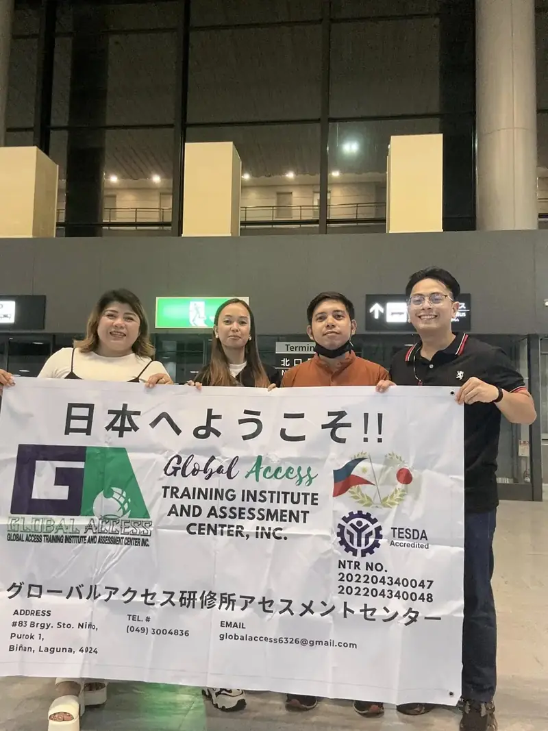 Four people holding a 日本へようこそ banner that shows the training center's registration details
