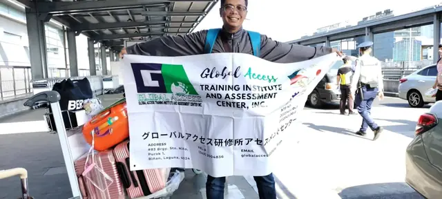Man holding the GLOBAL ACCESS banner outdoors beside a luggage trolley