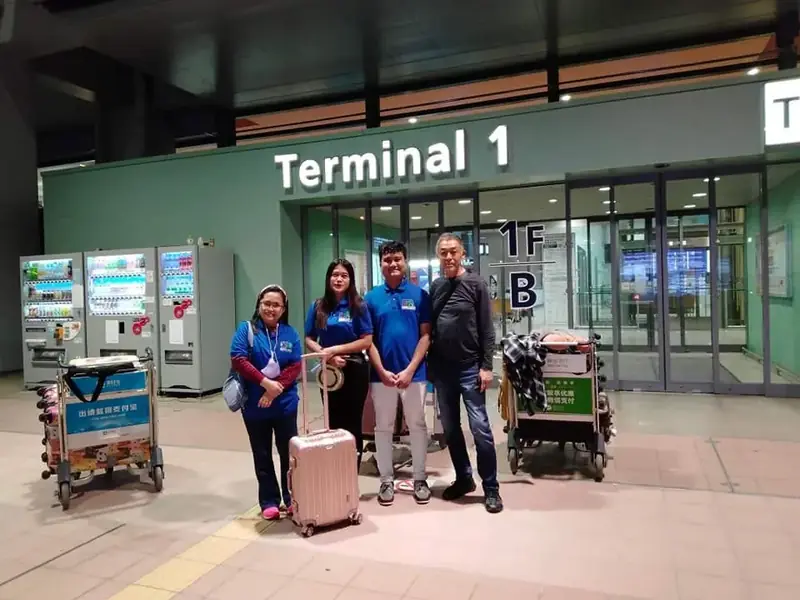 Participants in blue GLOBAL ACCESS shirts with luggage carts at the Terminal 1 entrance