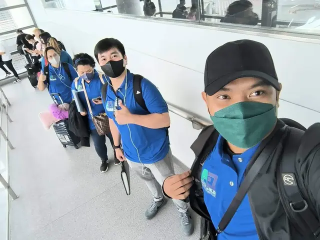 Participants in blue shirts riding a moving walkway in the terminal