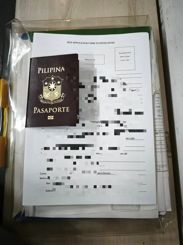 Passport on top of a folder of visa paperwork with personal details pixelated