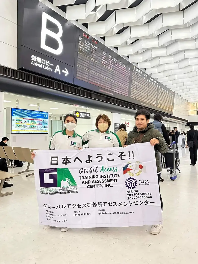 Staff holding a Welcome to Japan banner in front of the flight information board